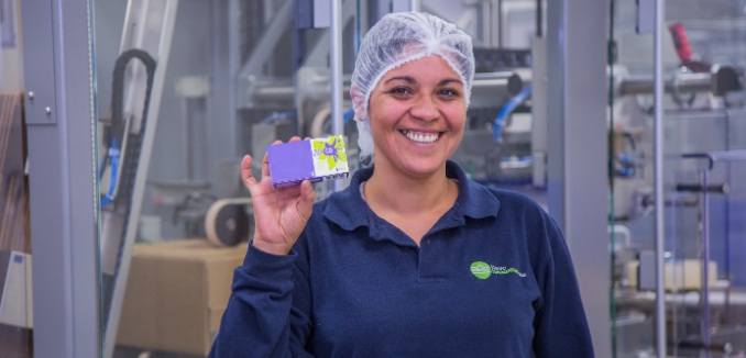 Trabajadora de una planta farmacéutica mostrando un medicamento en la mano y sonriendo