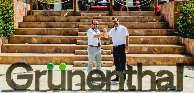 Dos hombres dándose la mano junto al logo de Grünenthal, sonriendo y mirando a la cámara