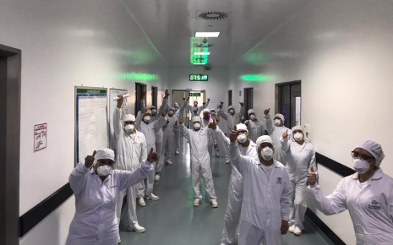 Grupo de farmacéuticos levantando los brazos en un pasadizo de una planta
